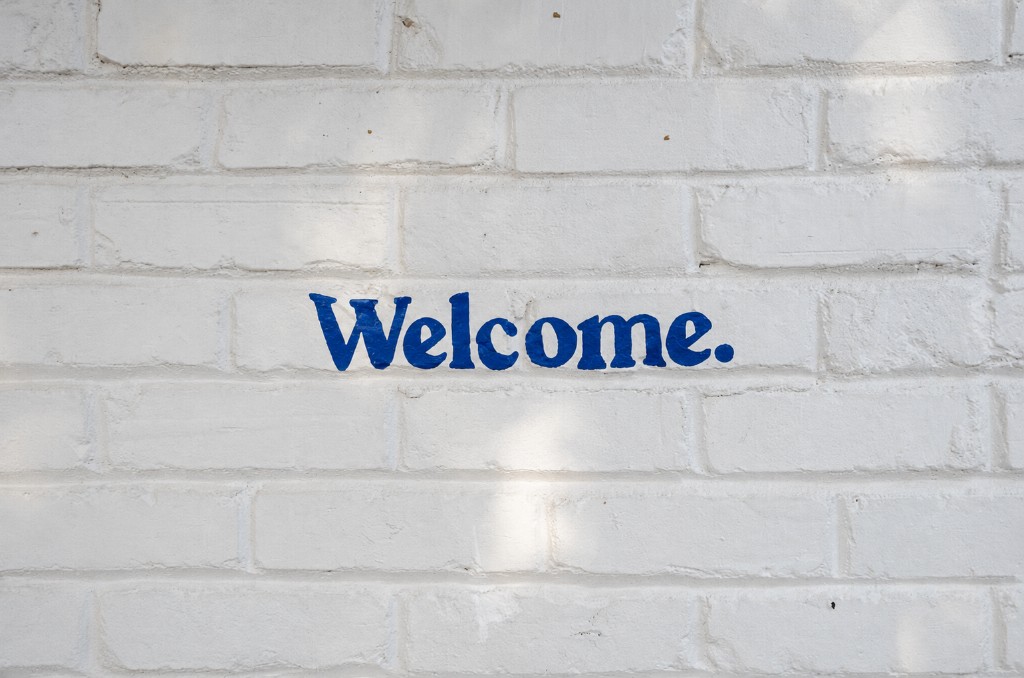 Welcome painted in blue on a white brick wall